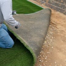 a photo of a turf installer laying turf over a prepared base material