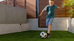 a photo of a boy kicking a soccer ball on the turf in his backyard