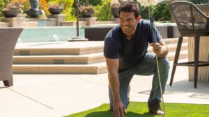 a photo of a happy golfer kneels to touch the soft turf on a backyard putting green