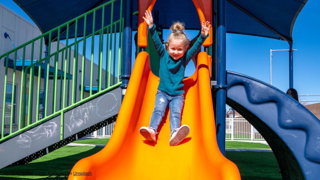 a young girl sliding down a backyard slide on synthetic turf